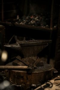 Close-up of an ancient blacksmith anvil on a wooden stump in a dimly lit workshop.